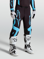 Alpinestars Pantalon Supertech Vesta, pantalon de motocross pour homme, noir et turquoise, tissu rip-stop extensible, panneaux en cuir de chèvre aux genoux, porté avec bottes blanches