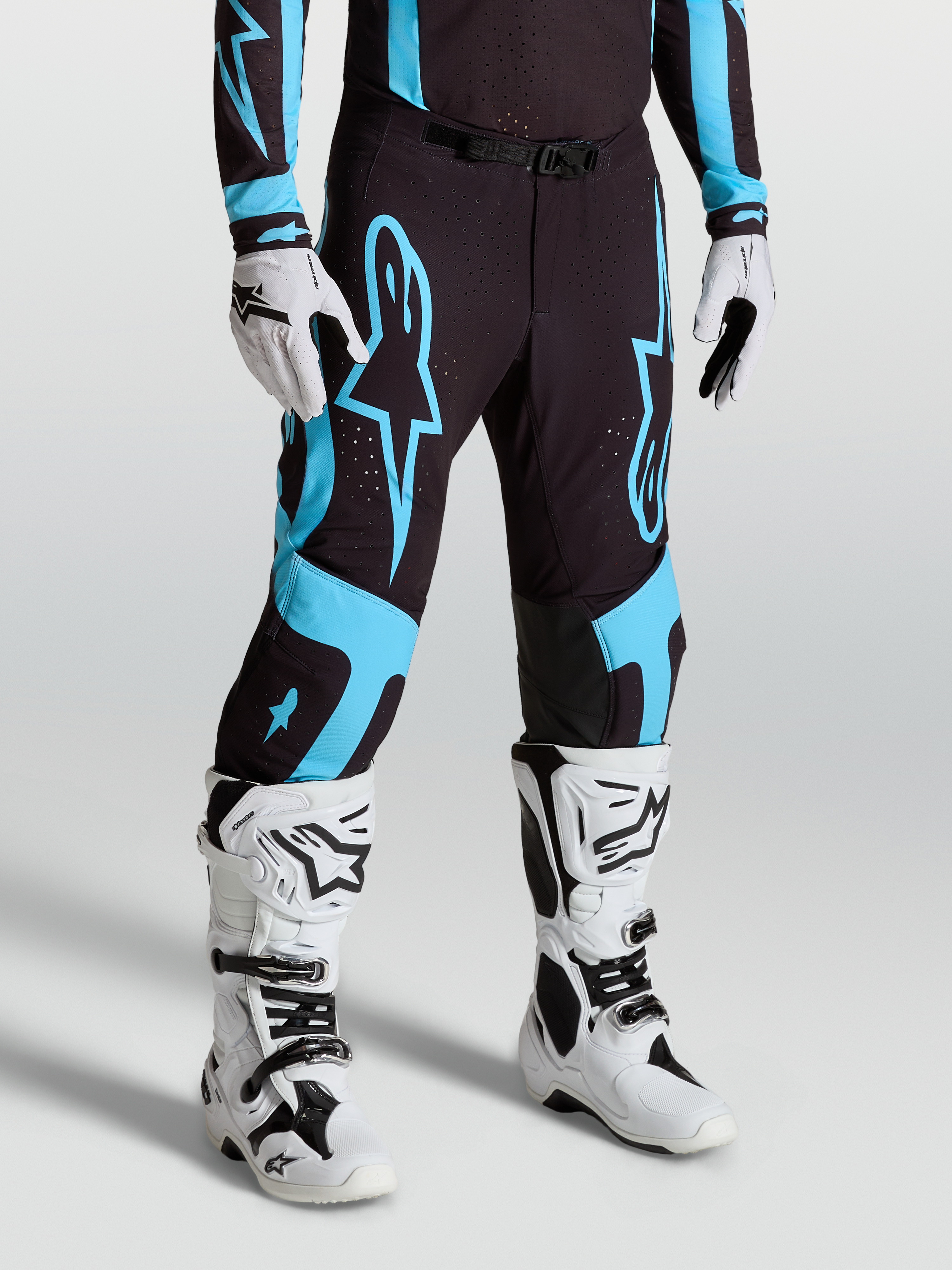 Alpinestars Pantalon Supertech Vesta, pantalon de motocross pour homme, noir et turquoise, tissu rip-stop extensible, panneaux en cuir de chèvre aux genoux, porté avec bottes blanches