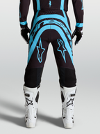 Pantalon Supertech Vesta Alpinestars, pantalon de motocross noir et turquoise avec bottes de moto off-road blanches, vue de dos montrant la coupe athlétique de course performance
