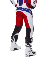 Alpinestars 2025 Racer Veil Pants, pantalon de motocross, rouge vif et blanc avec logo bleu, vue arrière montrant des empiècements de ventilation noirs extensibles à l'arrière des jambes, associé à des bottes de motocross blanches
