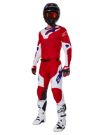 Alpinestars 2025 Racer Veil Pants, pantalon de motocross, rouge vif et blanc, porté dans le cadre d'un équipement de course complet comprenant un maillot rouge et blanc assorti, un casque noir avec des lunettes orange, des bottes blanches et des gants rouges, avec des logos Alpinestars bleus.