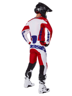 Alpinestars 2025 Racer Veil Pants, pantalon de motocross, rouge vif et blanc avec accents bleus, vu de dos sur un pilote en tenue complète, avec marquage Alpinestars audacieux, empiècements respirants sur le bas des jambes, bottes blanches et casque noir coordonnés.