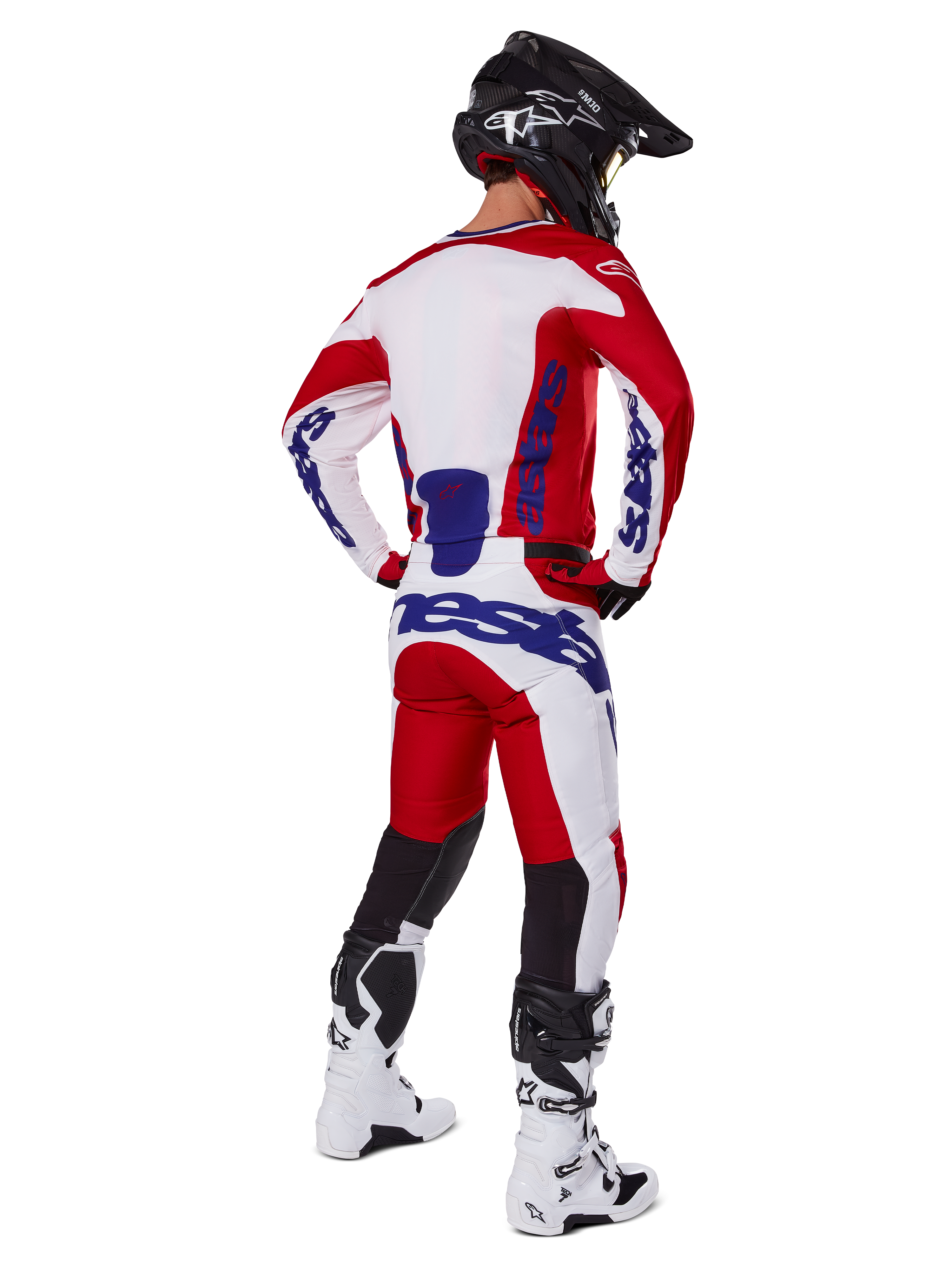 Alpinestars 2025 Racer Veil Pants, pantalon de motocross, rouge vif et blanc avec accents bleus, vu de dos sur un pilote en tenue complète, avec marquage Alpinestars audacieux, empiècements respirants sur le bas des jambes, bottes blanches et casque noir coordonnés.