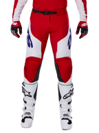 Alpinestars 2025 Racer Veil Pants, pantalon de motocross, rouge vif et blanc, porté avec des gants rouges assortis et des bottes blanches, doté de logos bleus sur les cuisses et d'une ceinture noire, coupe sport ergonomique pour le pilotage de performance
