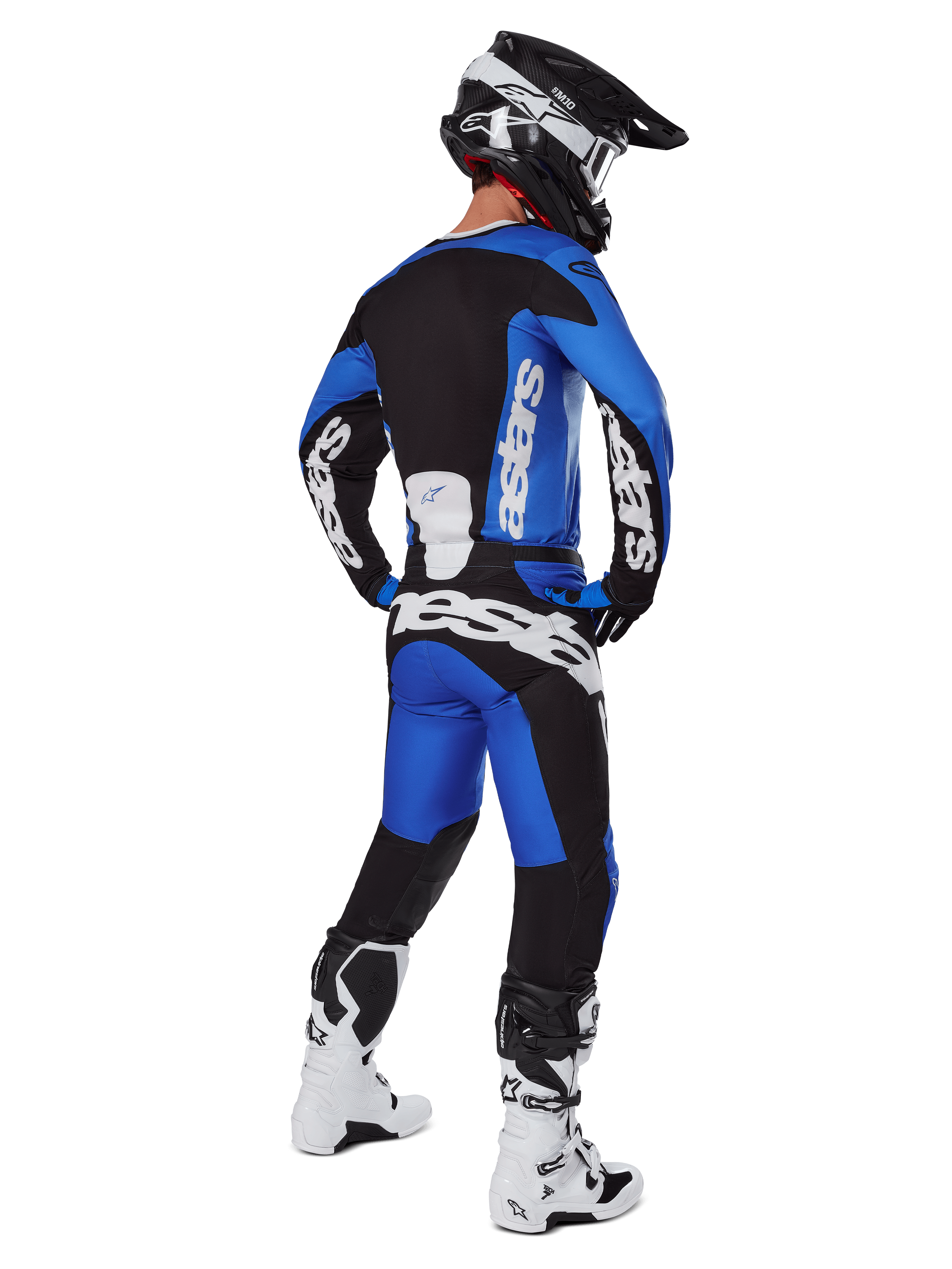 Motocross rider viewed from behind wearing Alpinestars 2025 Racer Veil Pants in Blue and Black, matching long-sleeve jersey with white branding, white and black Tech 7 boots, and a black SM10 helmet, full off-road racing gear set