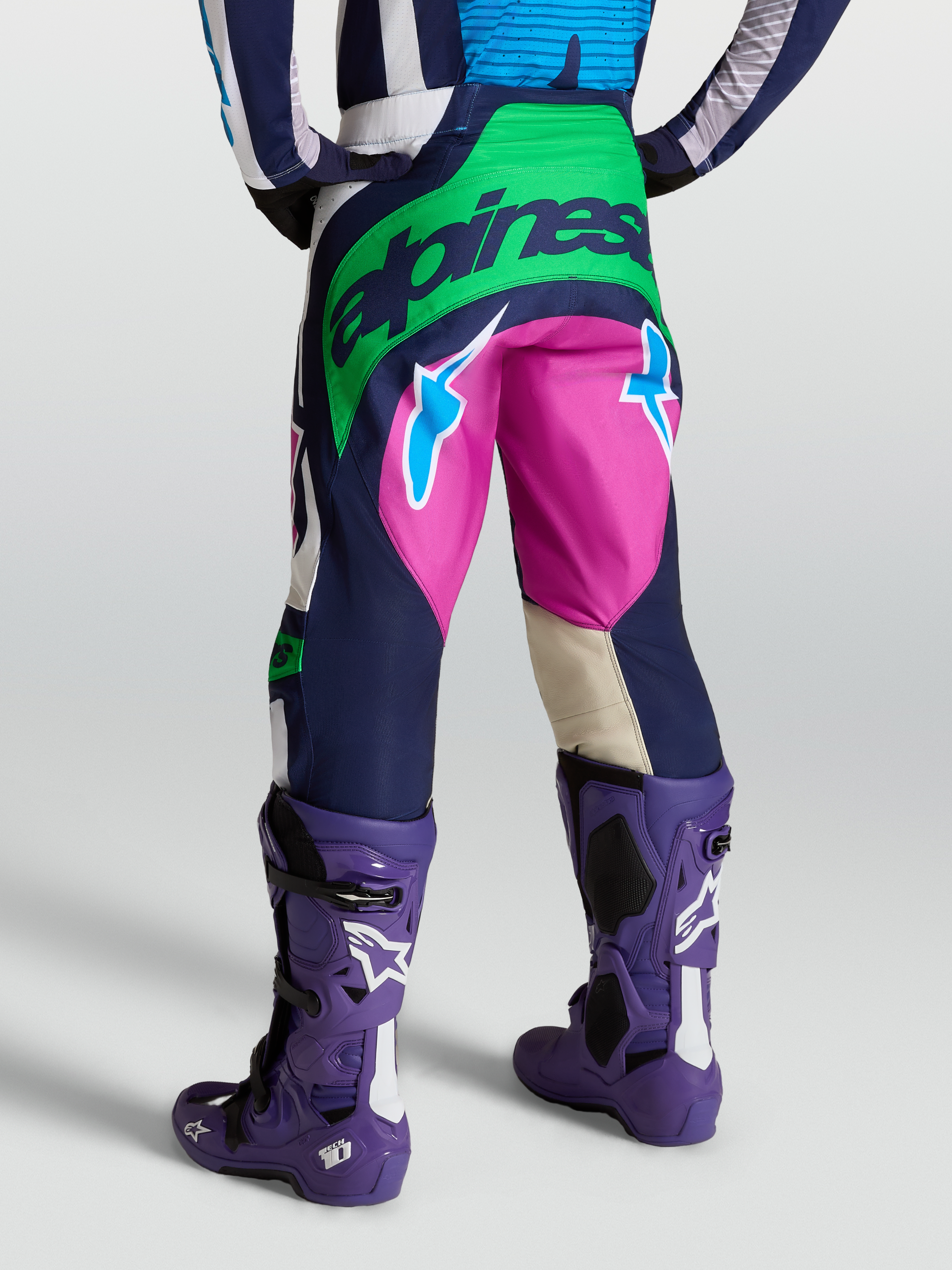 Alpinestars Pantalon Techstar Maven, équipement motocross bleu et vert, vue arrière avec bottes Tech 10 violettes.