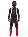 Ensemble d'équipement Alpinestars 2025 Fluid Haul, pilote de motocross en tenue de course complète, maillot noir avec accents rouges aux épaules et logos blancs, pantalon noir avec logo étoile blanc, bottes rouge vif, gants rouges et noirs, casque noir avec lunettes blanches, look de performance tout-terrain coordonné