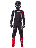 Ensemble d'équipement Alpinestars 2025 Fluid Haul, pilote de motocross en tenue de course complète, maillot noir avec accents rouges aux épaules et logos blancs, pantalon noir avec logo étoile blanc, bottes rouge vif, gants rouges et noirs, casque noir avec lunettes blanches, look de performance tout-terrain coordonné