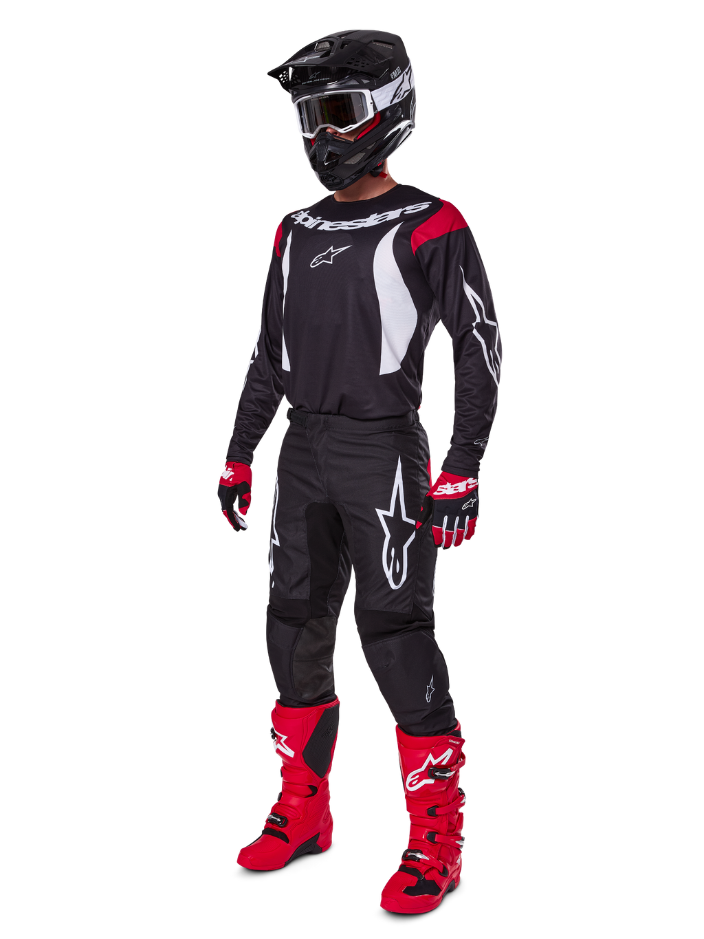Pilote de motocross portant l'ensemble d'équipement complet Alpinestars Fluid Haul 2025, maillot noir avec accents rouges et blancs, pantalon noir avec logos blancs, bottes rouge vif, gants rouges et noirs, casque noir avec lunettes, tenue de performance tout-terrain coordonnée