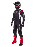 Pilote de motocross portant l'ensemble d'équipement complet Alpinestars Fluid Haul 2025, maillot noir avec accents rouges et blancs, pantalon noir avec logos blancs, bottes rouge vif, gants rouges et noirs, casque noir avec lunettes, tenue de performance tout-terrain coordonnée
