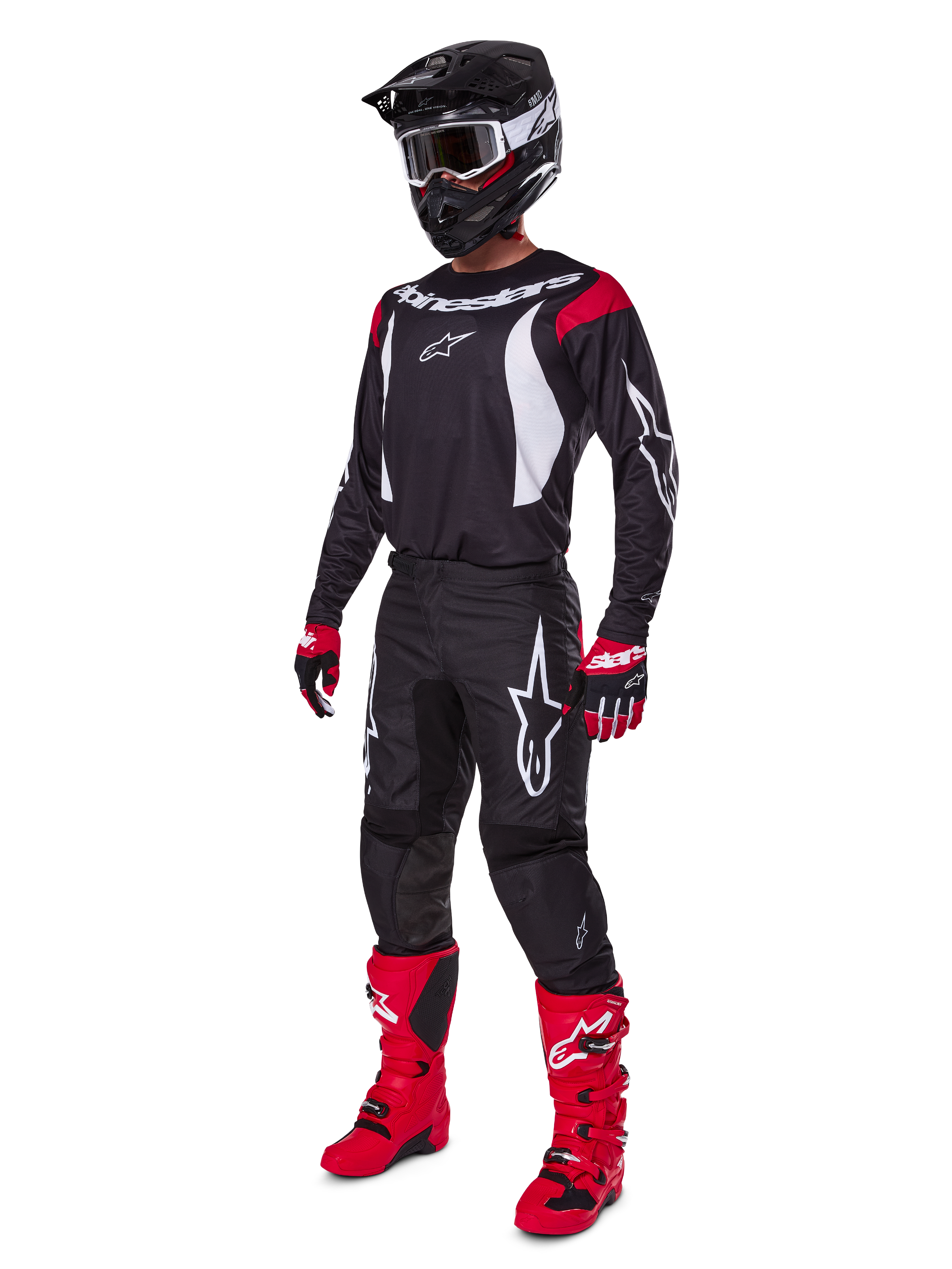 Pilote de motocross portant l'ensemble d'équipement complet Alpinestars Fluid Haul 2025, maillot noir avec accents rouges et blancs, pantalon noir avec logos blancs, bottes rouge vif, gants rouges et noirs, casque noir avec lunettes, tenue de performance tout-terrain coordonnée