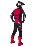 Pilote de motocross portant l'ensemble d'équipement Alpinestars 2025 Fluid Haul vu de dos, maillot rouge et noir avec marquage blanc, pantalon noir assorti avec accents rouges, bottes rouge vif et casque noir avec lunettes blanches, tenue coordonnée complète pour la course tout-terrain