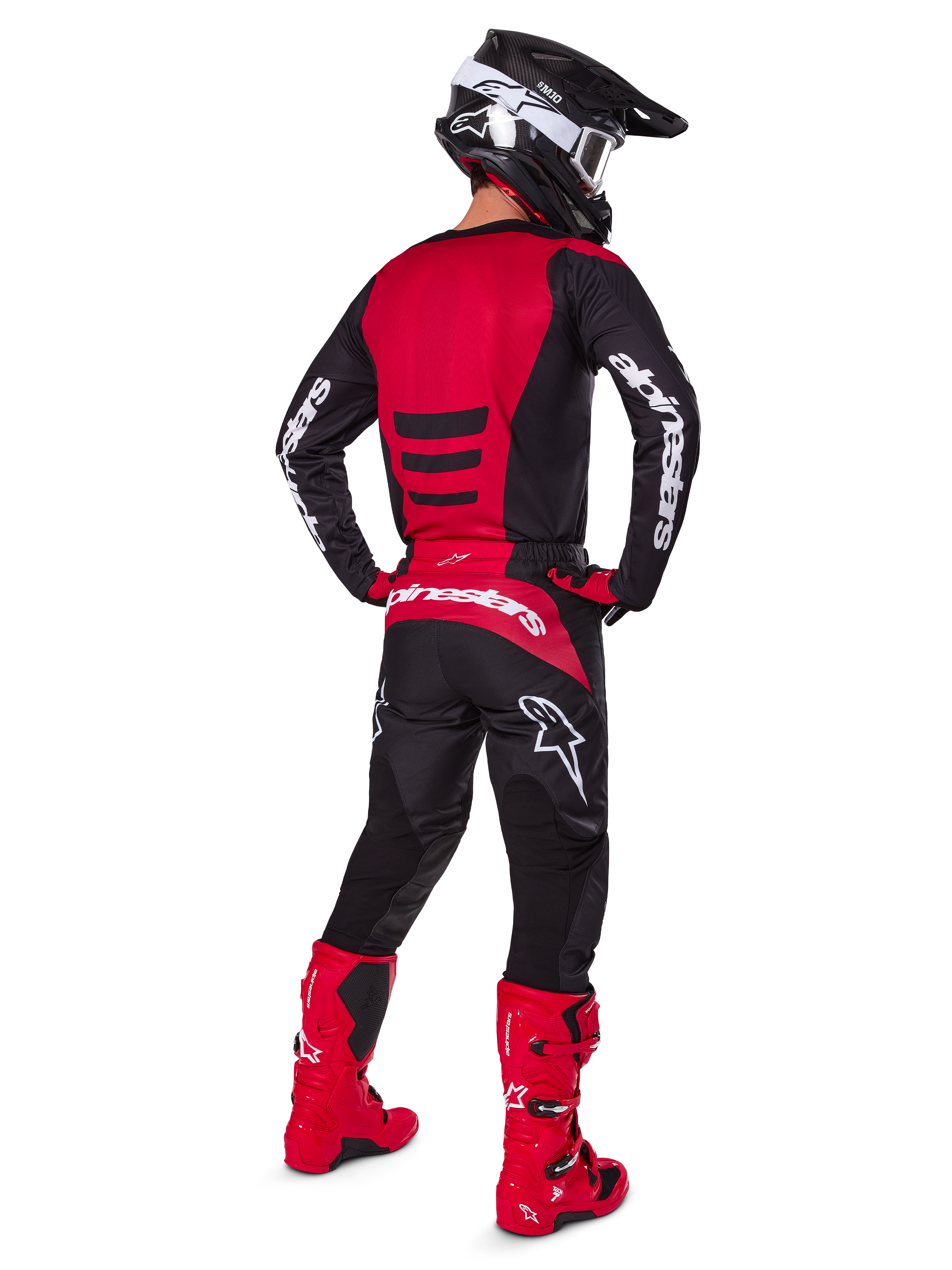 Pilote de motocross portant l'ensemble d'équipement Alpinestars 2025 Fluid Haul vu de dos, maillot rouge et noir avec marquage blanc, pantalon noir assorti avec accents rouges, bottes rouge vif et casque noir avec lunettes blanches, tenue coordonnée complète pour la course tout-terrain