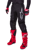 Alpinestars 2025 Fluid Haul Pants, pantalon de motocross, noir, avec un grand logo Alpinestars blanc, porté avec des bottes rouge vif et des gants rouges et noirs, construction durable en poly-tissu 600D avec coupe ergonomique pour la course tout-terrain