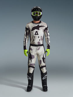 Motocross rider wearing the Alpinestars 2026 Racer Lahnd Gear Set, Sand Camo patterned suit with white, gray, and black design, black helmet with neon green goggles, bright neon green gloves, and black boots with white logos, complete coordinated outfit for off-road racing