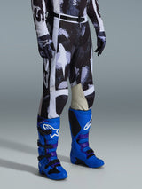 Pantalon Alpinestars Racer Lahnd 2026, pantalon de motocross, motif camouflage Iron Camo gris et noir, porté avec des bottes de course bleu vif et des gants assortis, doté de panneaux blancs et de genoux intérieurs en cuir de chèvre, équipement tout-terrain axé sur la performance