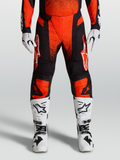 Alpinestars Pantalons Techstar Swan 2027, pantalons de motocross rouges et noirs, portés avec des bottes de moto et des gants blancs, équipement de protection pour le tout-terrain.