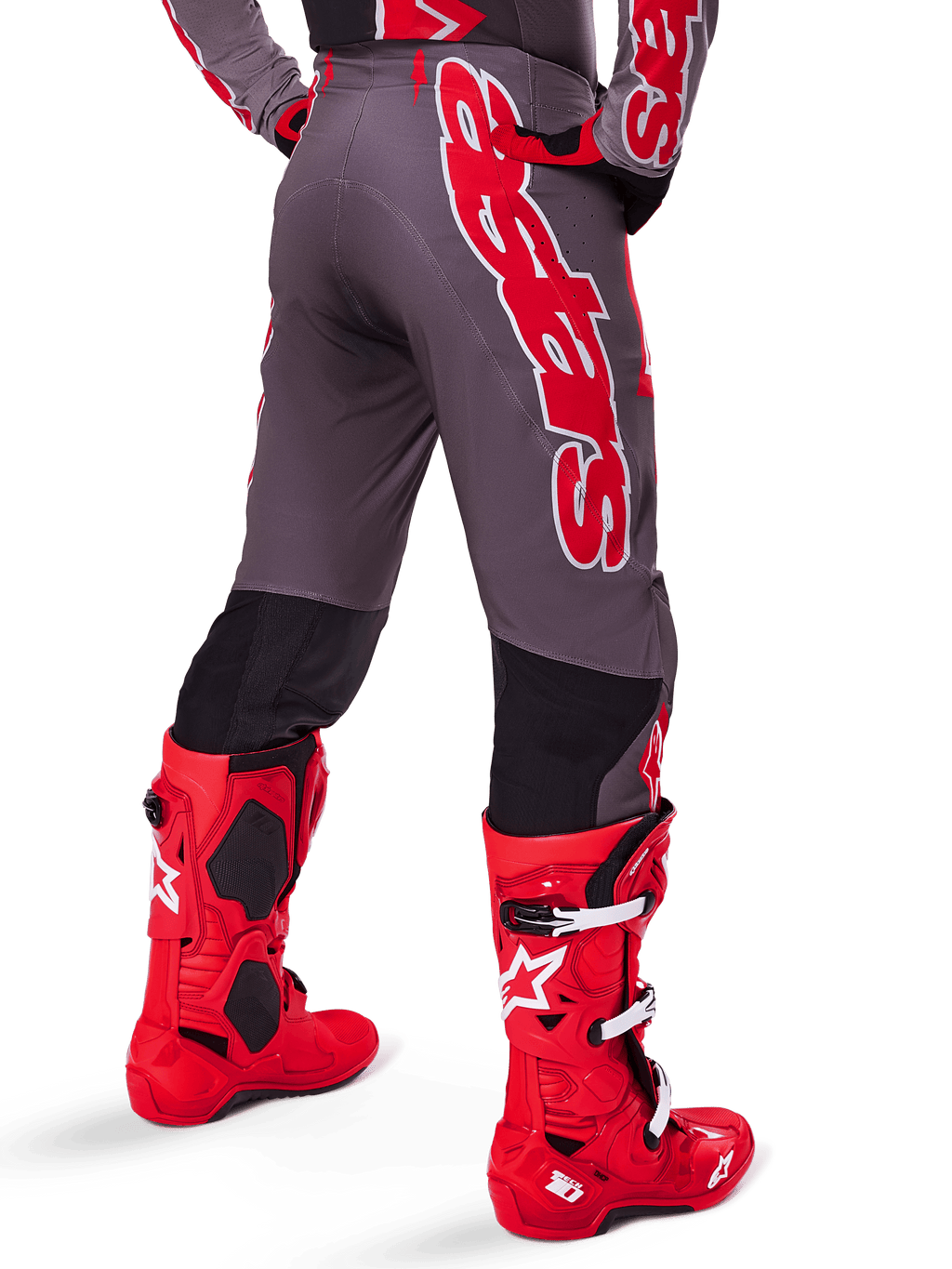 Ensemble d'équipement Alpinestars Supertech Lipan 2025, vue arrière d'un pilote de motocross, pantalon gris foncé avec large marquage vertical rouge, maillot assorti rouge et gris, bottes de motocross rouge vif, équipement de course tout-terrain haute performance