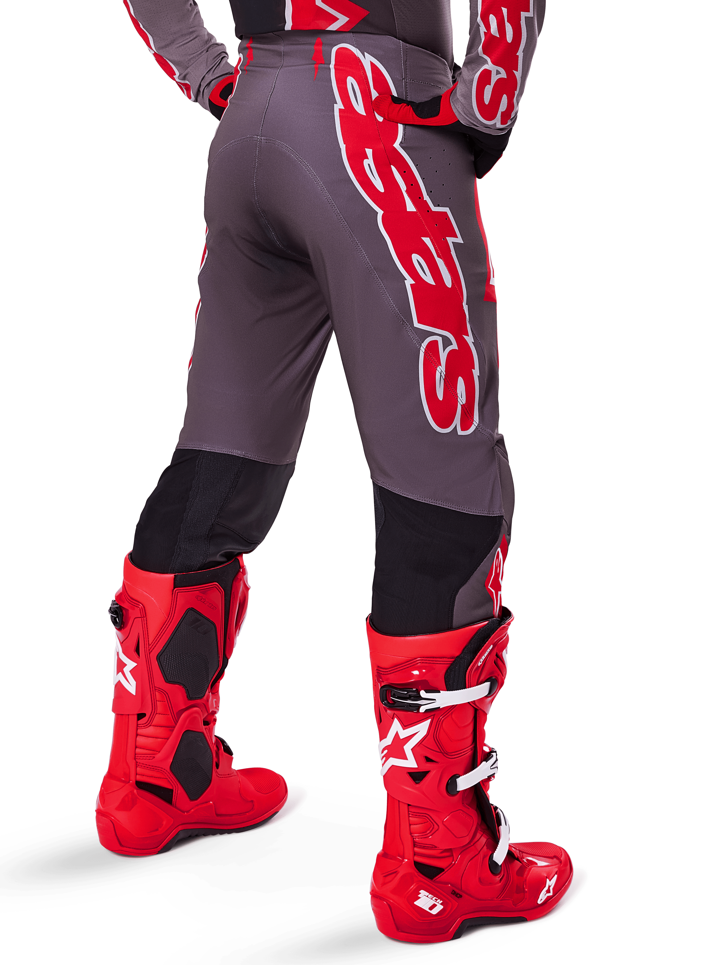Ensemble d'équipement Alpinestars Supertech Lipan 2025, vue arrière d'un pilote de motocross, pantalon gris foncé avec large marquage vertical rouge, maillot assorti rouge et gris, bottes de motocross rouge vif, équipement de course tout-terrain haute performance