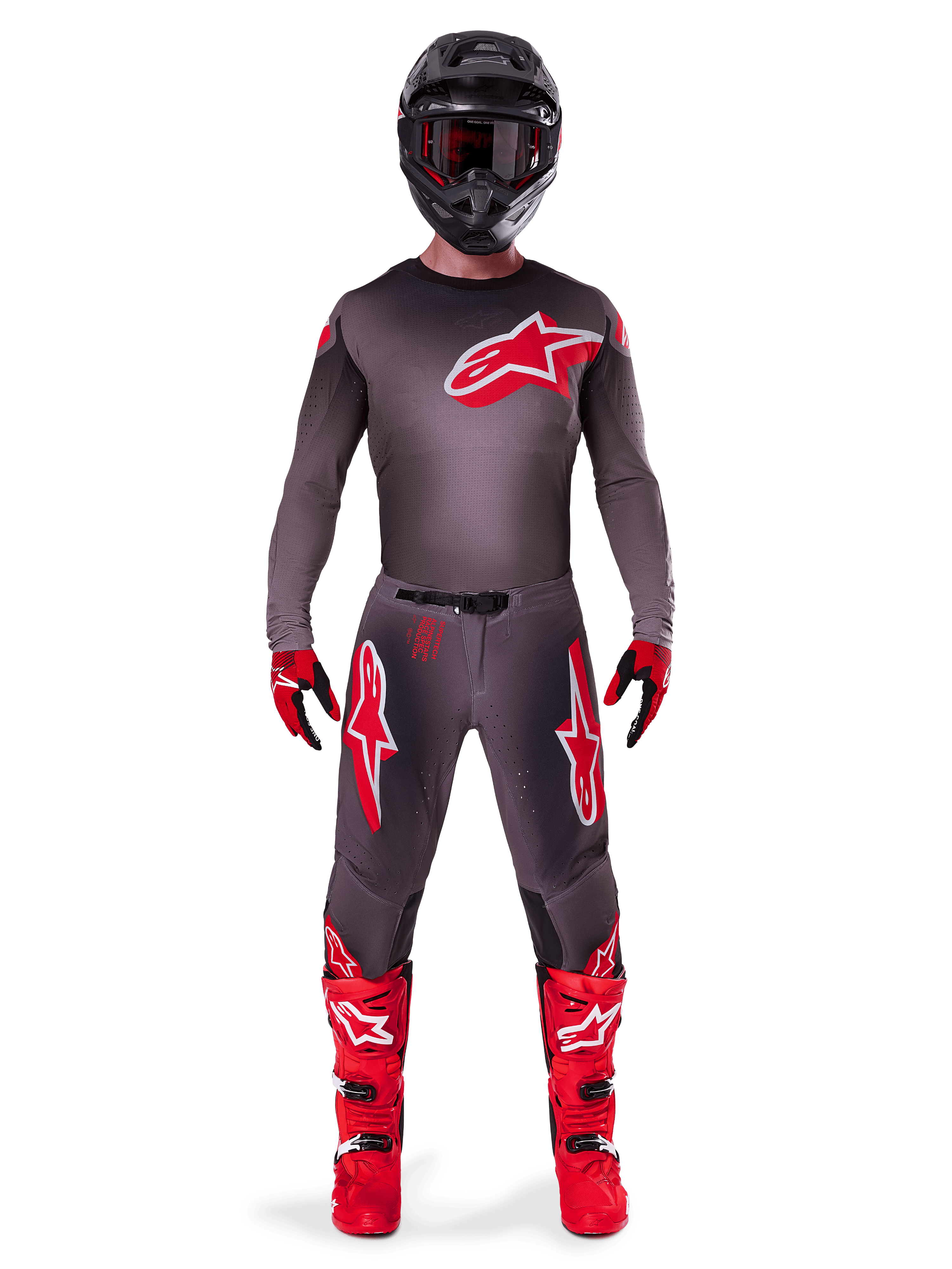 Pilote de motocross portant la tenue complète Alpinestars Supertech Lipan 2025, coloris Smoke Bright Red, comprenant un maillot et un pantalon gris foncé avec des logos rouges proéminents, un casque noir avec lunettes, des gants rouges et noirs et des bottes de motocross rouge vif, tenue de course professionnelle coordonnée.