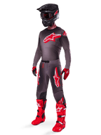 Pantalon Alpinestars Supertech Lipan 2025, pantalon de motocross, Smoke Bright Red, base gris foncé avec de grands logos Alpinestars rouges sur les cuisses, porté avec maillot assorti, casque noir, gants rouges et noirs et bottes rouge vif, tenue de motocross professionnelle coordonnée