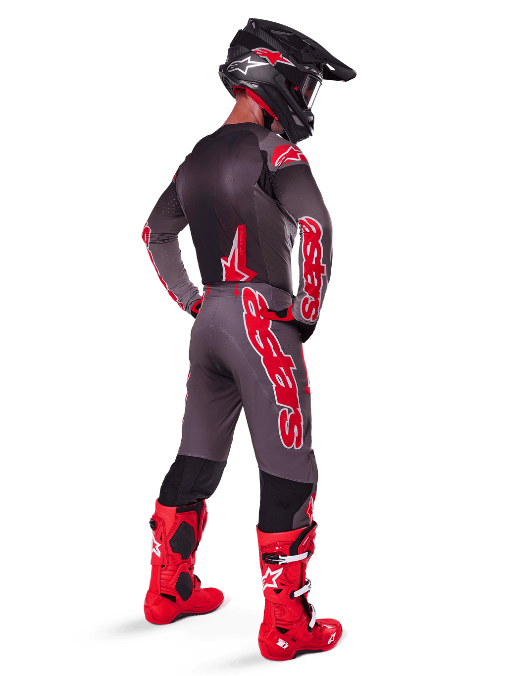 Pilote de motocross portant le pantalon Alpinestars Supertech Lipan 2025, Smoke Bright Red, pantalon gris avec de grands logos rouges et des panneaux intérieurs noirs aux jambes, associé à un maillot gris assorti, un casque noir et des bottes rouge vif, tenue de course tout-terrain complète vue de dos.