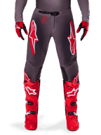 Alpinestars Supertech Lipan Pants 2025, pantalon de motocross, Smoke Bright Red, châssis gris avec logos rouges et blancs proéminents, porté avec bottes et gants de course rouges, doté de ventilations perforées, équipement tout-terrain haute performance