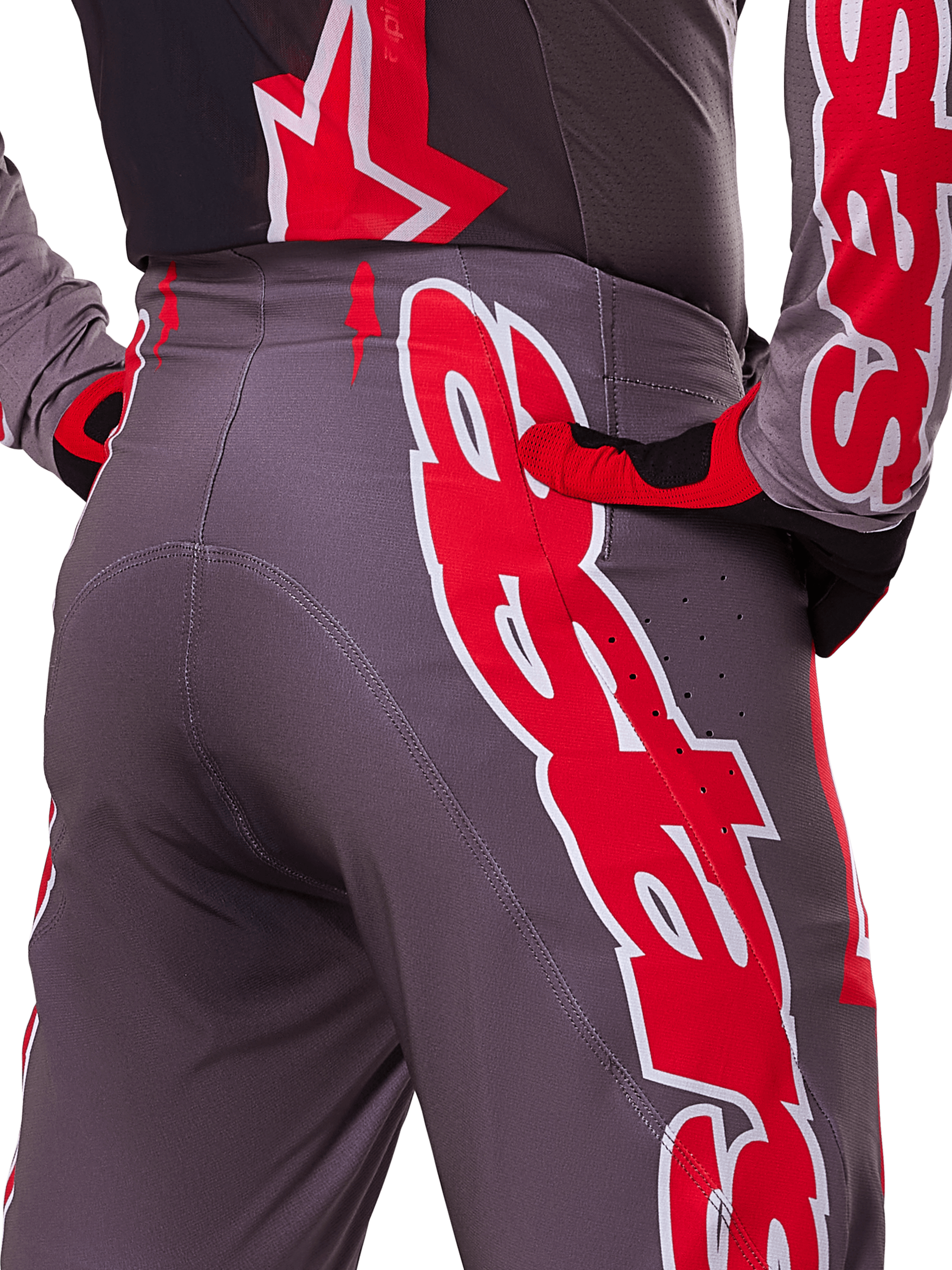 Pantalon Alpinestars Supertech Lipan 2025, pantalon de motocross, rouge vif et gris, gros plan sur la hanche et l'arrière montrant des logos rouges et blancs audacieux, perforations de ventilation, et coupe athlétique de course portée avec la tenue assortie.
