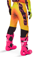 Ensemble d'équipement Alpinestars Supertech Lipan 2025, vue arrière du pantalon de motocross avec dégradé jaune et orange et marquage noir imposant, associé à des bottes Tech 10 rose vif et des gants jaunes, équipement de course tout-terrain professionnel