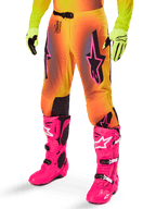 Alpinestars 2025 Supertech Lipan Gear Set, pantalon de motocross, dégradé jaune et orange avec accents rose et violet, logos Alpinestars noirs sur les cuisses, porté avec des gants jaunes et des bottes de motocross rose vif.