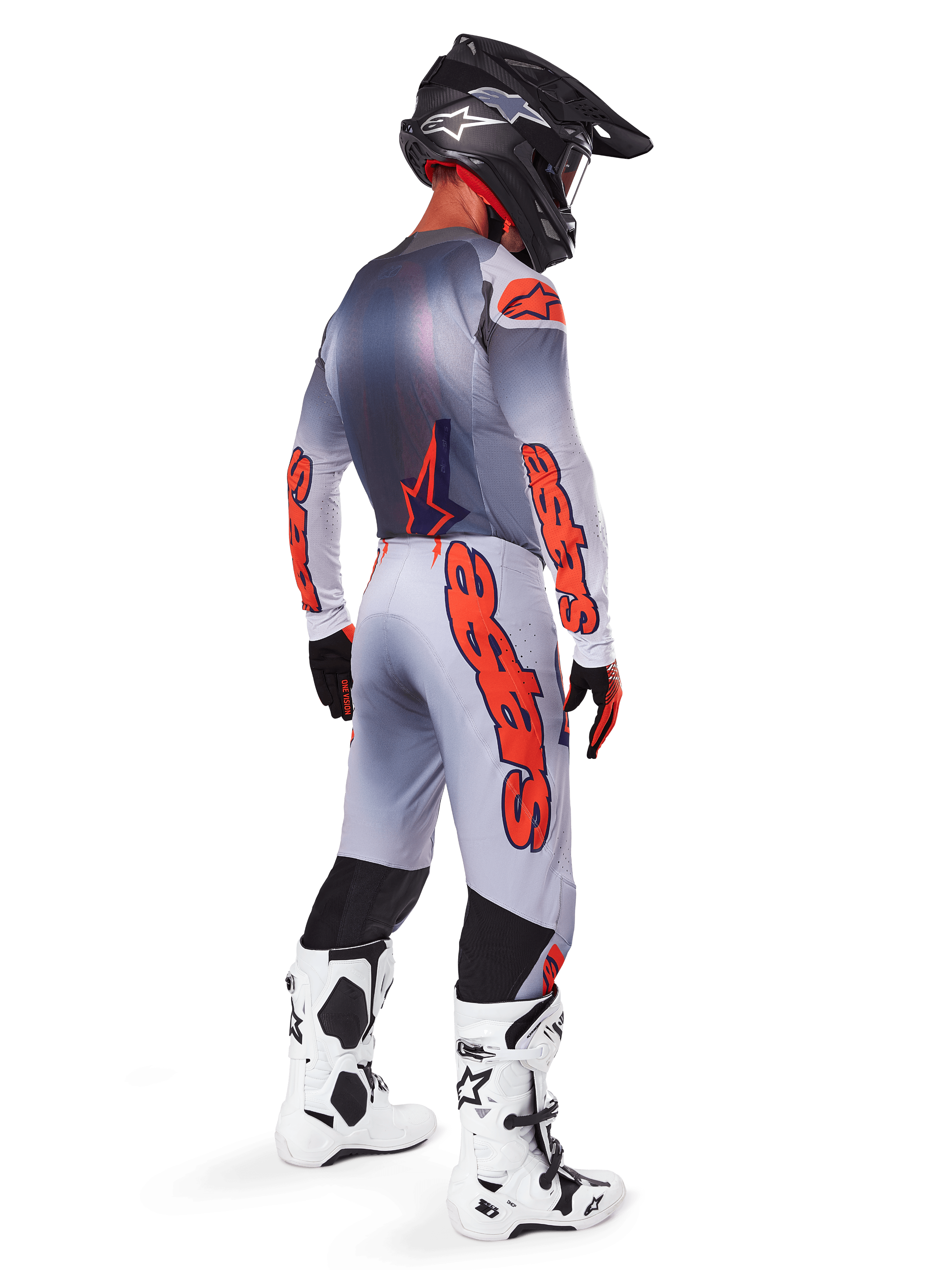 Pilote de motocross vu de dos portant le pantalon Alpinestars Supertech Lipan 2025 en gris et orange fluo, maillot à manches longues assorti, casque noir et bottes techniques blanches et noires, équipement complet de course tout-terrain professionnel.