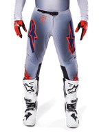 Alpinestars 2025 Supertech Lipan Pants, pantalon de motocross, gris et orange fluo, porté avec des gants rouges et noirs et des bottes blanches et noires, arborant de grands logos étoilés Alpinestars sur les cuisses et des perforations de ventilation pour la compétition de niveau professionnel.