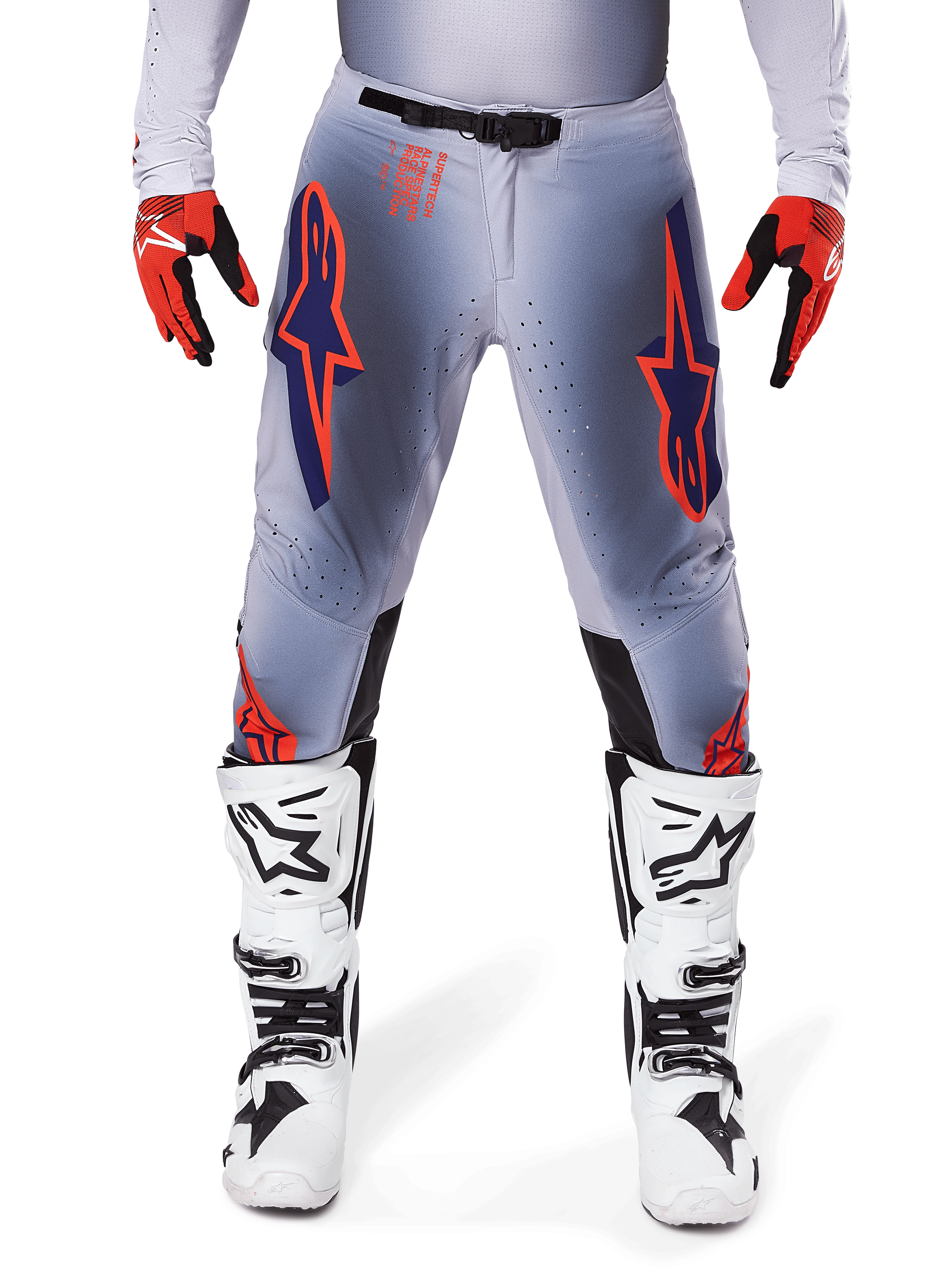Alpinestars 2025 Supertech Lipan Pants, pantalon de motocross, gris et orange fluo, porté avec des gants rouges et noirs et des bottes blanches et noires, arborant de grands logos étoilés Alpinestars sur les cuisses et des perforations de ventilation pour la compétition de niveau professionnel.