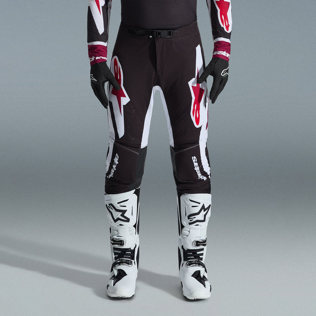 Alpinestars 2026 Supertech AFD Vista Gear Set, pilote de motocross portant un pantalon noir avec de grands logos blancs et rouges, maillot de performance assorti avec des poignets bordeaux, gants noirs et bottes de course professionnelles blanches, tenue de course tout-terrain haute performance
