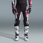 Alpinestars 2026 Supertech AFD Vista Gear Set, pilote de motocross portant un pantalon noir avec de grands logos blancs et rouges, maillot de performance assorti avec des poignets bordeaux, gants noirs et bottes de course professionnelles blanches, tenue de course tout-terrain haute performance