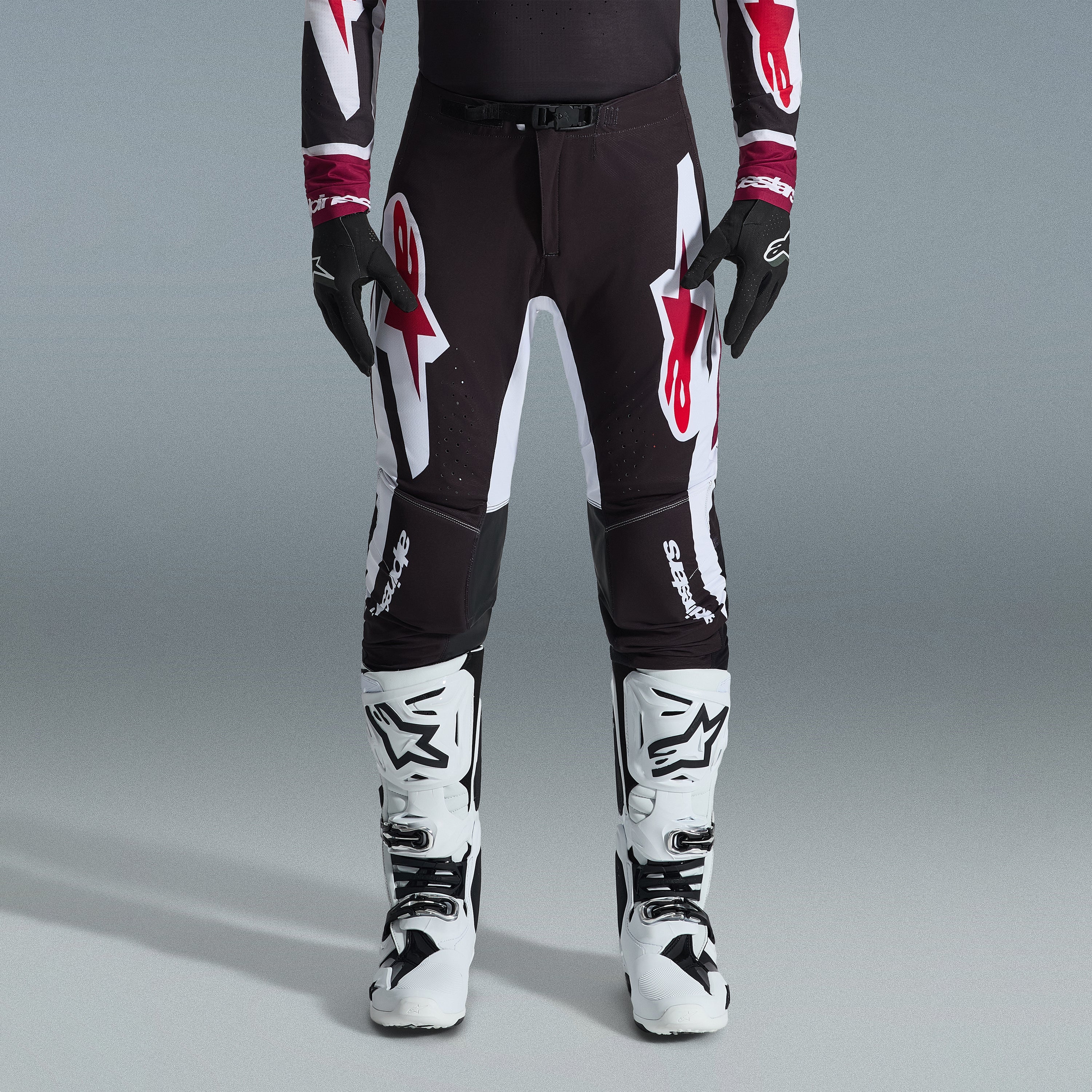 Alpinestars 2026 Supertech AFD Vista Gear Set, pilote de motocross portant un pantalon noir avec de grands logos blancs et rouges, maillot de performance assorti avec des poignets bordeaux, gants noirs et bottes de course professionnelles blanches, tenue de course tout-terrain haute performance