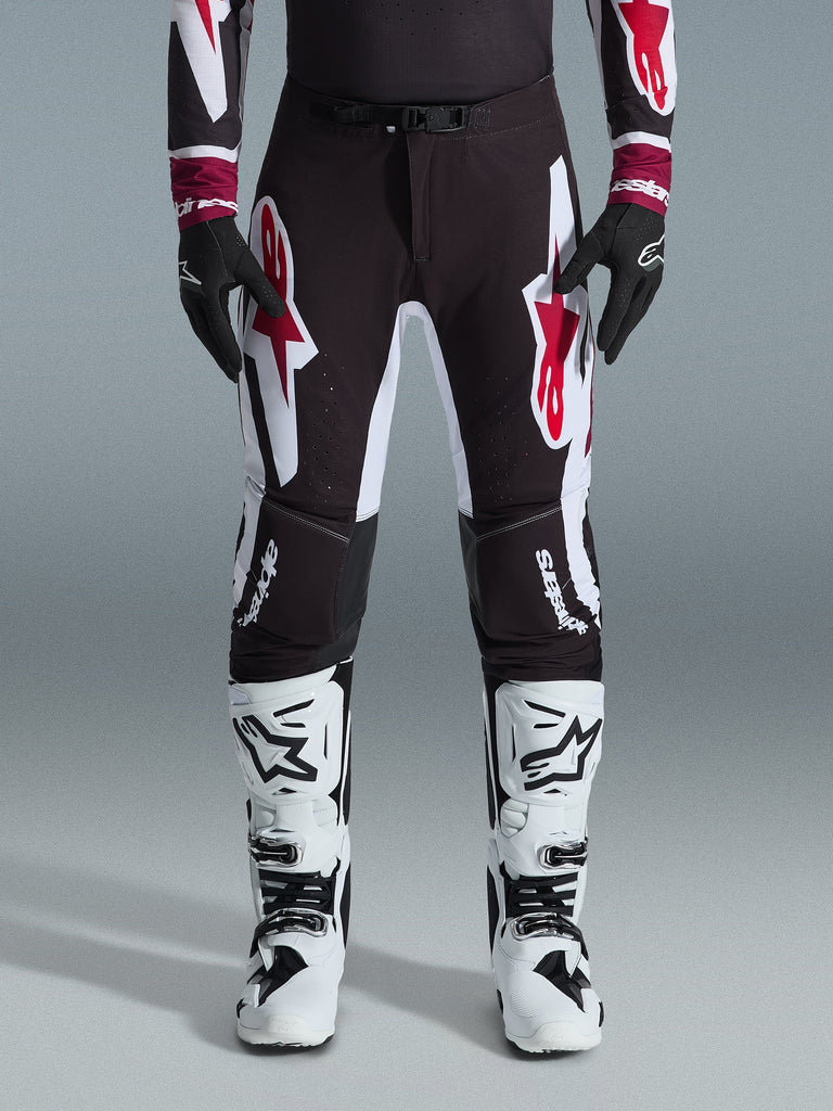 Alpinestars Supertech AFD Vista Pants 2026, pantalon de motocross, noir, rouge et blanc, avec de grands logos graphiques sur les cuisses et les genoux, porté avec des bottes de course blanches et des gants noirs, design athlétique prêt pour la compétition tout-terrain d'élite