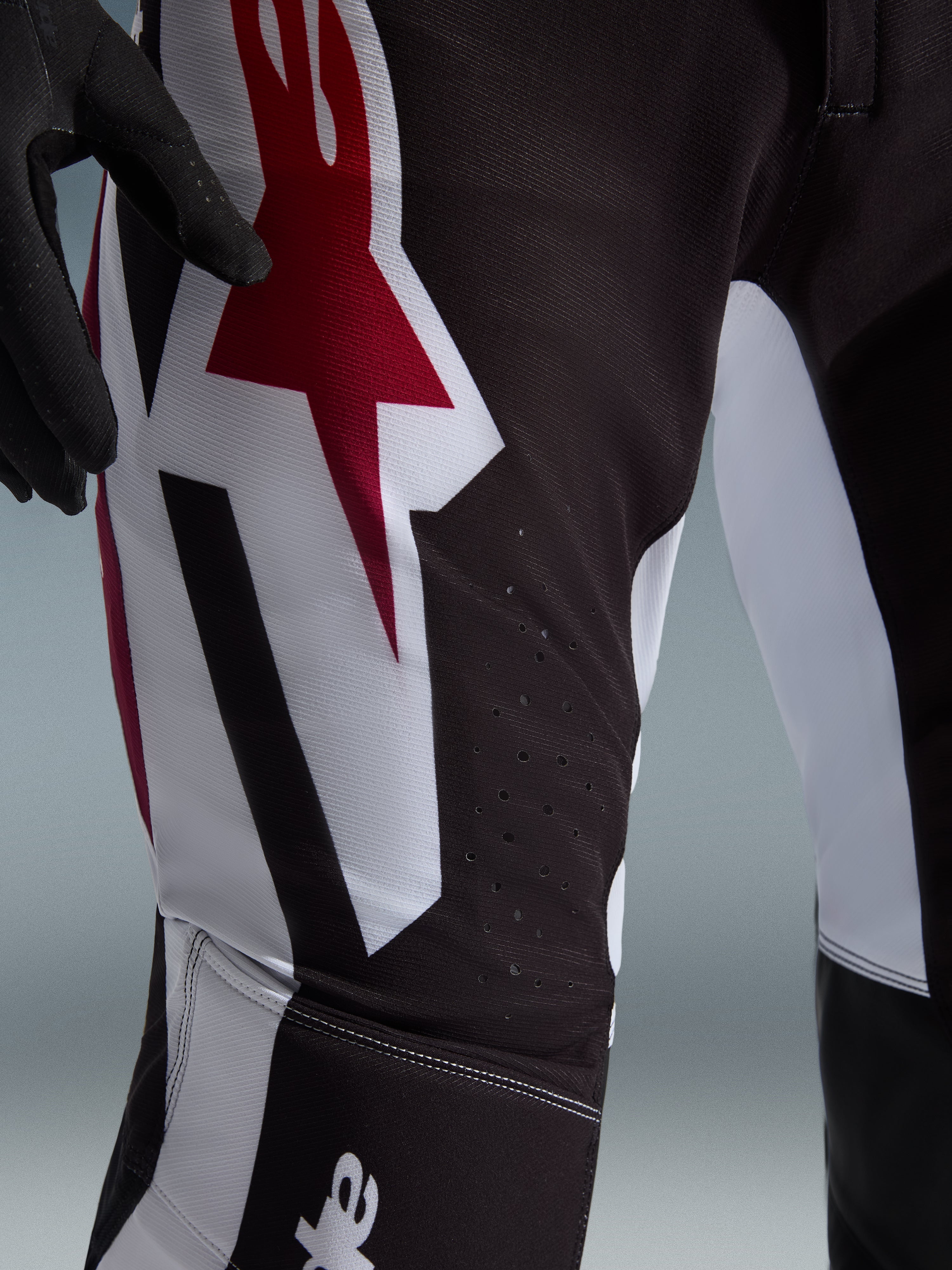 Alpinestars Supertech AFD Vista 2026, pantalon de motocross, noir, rouge et blanc, vue rapprochée de la cuisse présentant un grand logo Astars rouge et blanc et des perforations découpées au laser pour la ventilation.