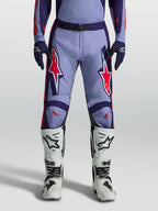 Alpinestars Racer Air Hunt, pantalons de motocross violets et rose fluo, portés avec des bottes blanches
