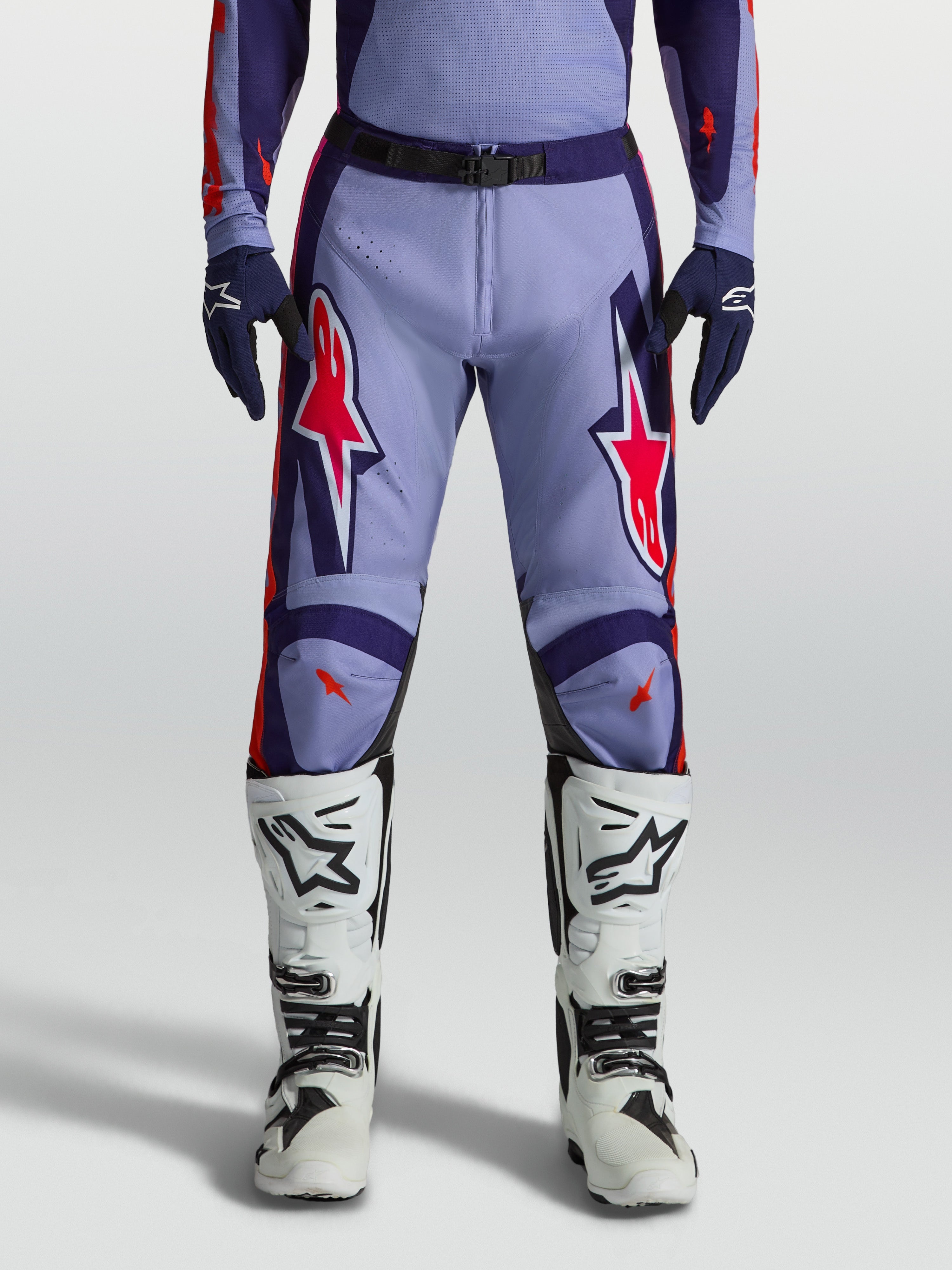 Alpinestars Racer Air Hunt, pantalons de motocross violets et rose fluo, portés avec des bottes blanches