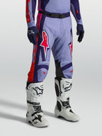 Alpinestars pantalons Racer Air Hunt, équipement de motocross ventilé violet et rose, porté avec des bottes de moto blanches.