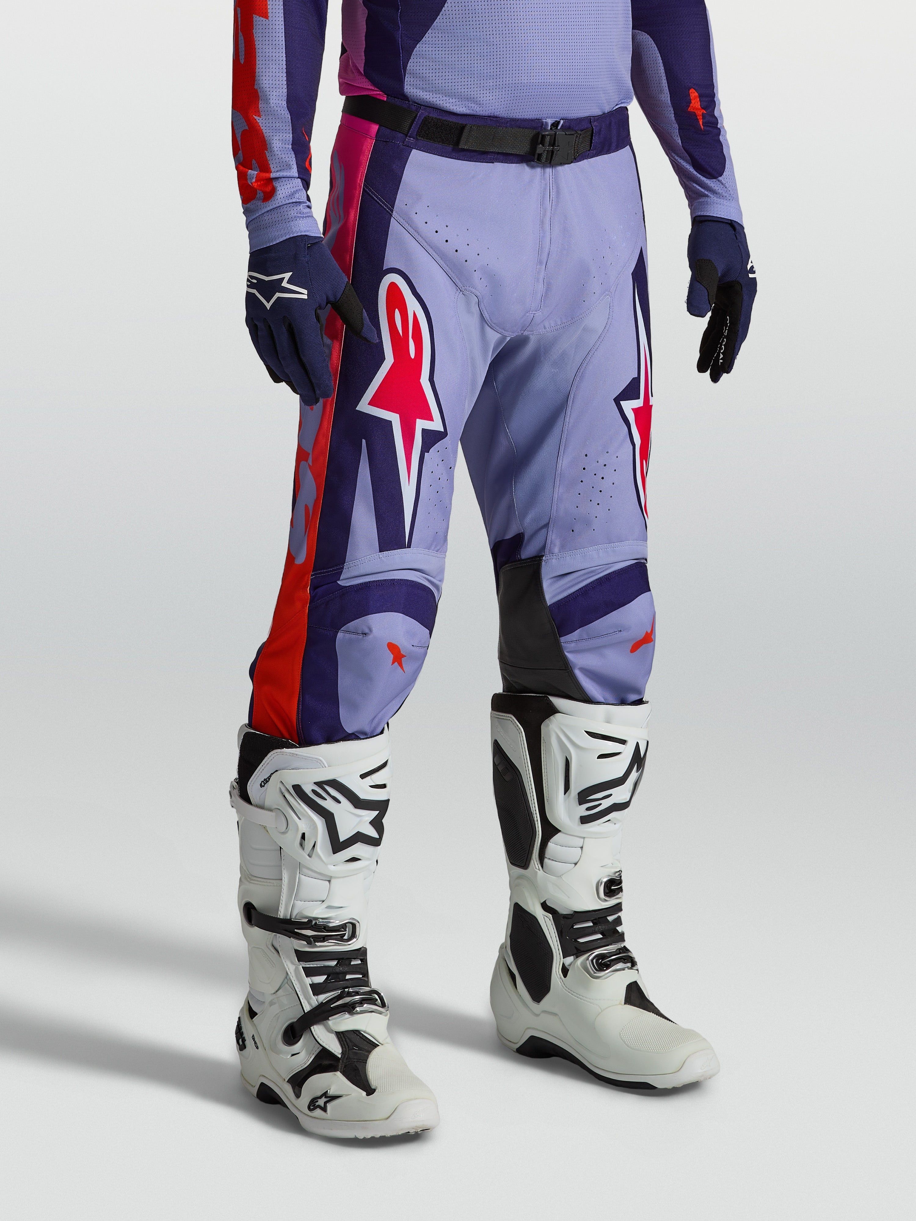 Alpinestars pantalons Racer Air Hunt, équipement de motocross ventilé violet et rose, porté avec des bottes de moto blanches.
