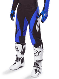 Alpinestars Techstar Dreem Pants 2025, pantalon de motocross noir et bleu, porté avec des bottes de motocross blanches et des gants bleus, avec logo Alpinestars blanc sur la jambe, construction durable pour la course tout-terrain