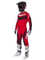 Pilote de motocross portant une tenue de course complète comprenant le pantalon Alpinestars Techstar Dreem 2025 rouge vif et noir, un maillot assorti rouge et noir avec logo blanc, un casque noir et des bottes blanches et noires, tenue coordonnée pour la course tout-terrain