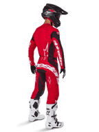 Pantalon Alpinestars Techstar Dreem 2025, pantalon de motocross, rouge vif et noir, porté par un pilote vu de dos dans une tenue de course complète avec maillot rouge assorti, casque noir et bottes blanches, avec logo Alpinestars blanc et empiècements extensibles noirs.