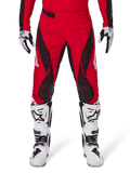 Pantalon Alpinestars Techstar Dreem 2025, pantalon de motocross rouge vif et noir avec motifs angulaires et perforations laser, porté avec des bottes de motocross blanches et des gants assortis pour la course tout-terrain