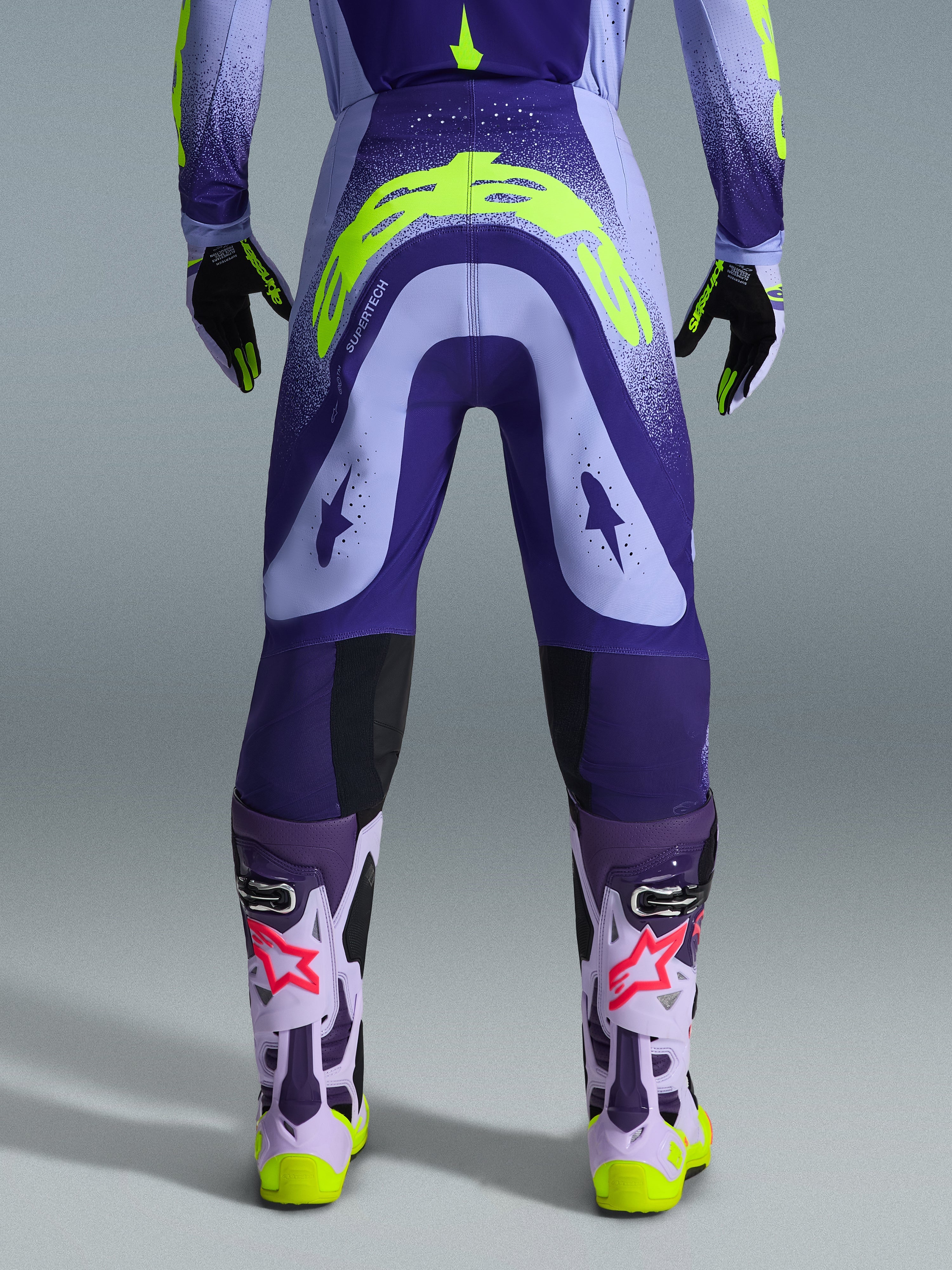 Alpinestars 2026 Supertech Scenz Pants, Motocross Pants, Purple and Yellow Fluo, rear view showing large yellow logo on seat, worn with matching jersey, gloves, and protective boots, athletic fit for professional motocross racing.