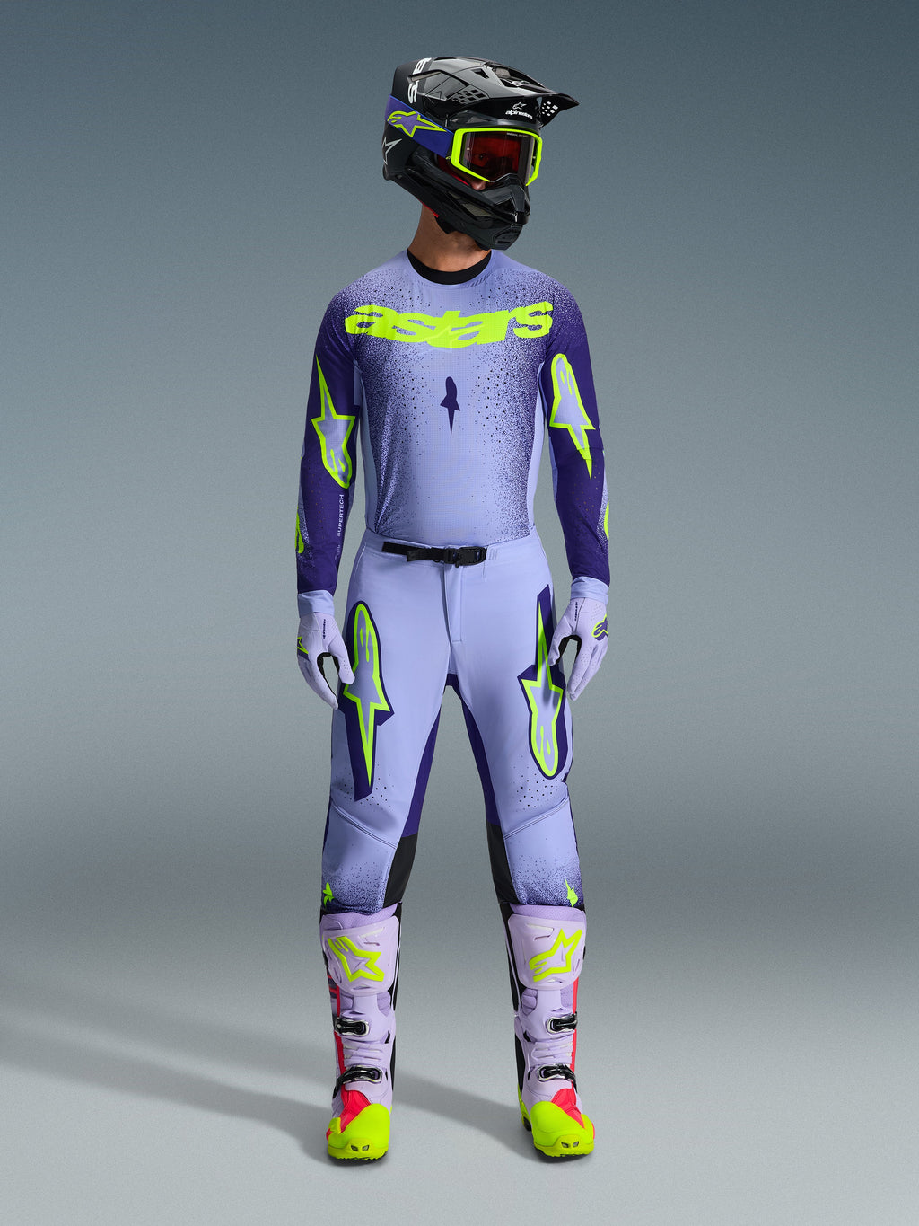 Ensemble d'équipement Alpinestars 2026 Supertech Scenz, tenue de course de motocross, violet clair et jaune-vert néon, équipement de protection complet comprenant un casque noir avec des accents violets, un maillot avec un marquage jaune néon audacieux, un pantalon assorti avec des graphismes d'étoiles et des bottes coordonnées avec des touches roses.
