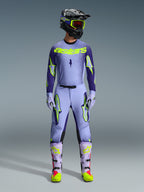 Ensemble d'équipement Alpinestars 2026 Supertech Scenz, tenue de course de motocross, violet clair et jaune-vert néon, équipement de protection complet comprenant un casque noir avec des accents violets, un maillot avec un marquage jaune néon audacieux, un pantalon assorti avec des graphismes d'étoiles et des bottes coordonnées avec des touches roses.