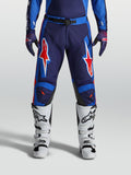 Alpinestars Pantalon Racer Hunt, pantalon de motocross pour homme, bleu et rouge, construction pré-courbée avec graphismes étoilés, porté avec des bottes blanches